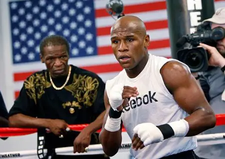 Floyd Mayweather Sr.. looking at his $565 million net worth son in the ring wearing a reebok vest from outside his corner.