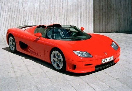 A red Koenigsegg CC8S parked in a concrete floor in front of a wall.