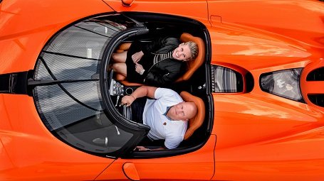 Christian von Koenigsegg and his wife, Halldora von Koenigsegg looking at the camera above their head while sitting on their red Koenigsegg car.