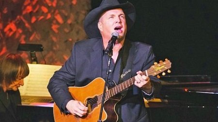 Garth Brooks singing his heart out with a guitar and a signature hat.