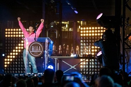 Garth Brooks received his 7th Diamond Certificate from the RIAA in 2016. Pink shirt and thowing his hands up in the air.