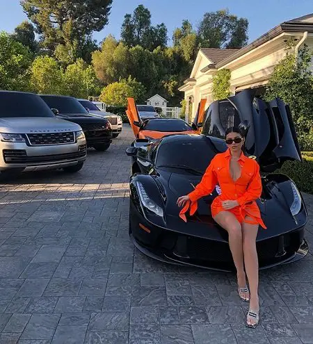 Kylie Jenner in front of a number of cars from her car collection while sitting on the front of the Aperta.