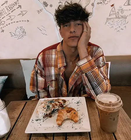 Tayler Holder at a restaurant in front of a plate of two croissants with his hand on his cheek.