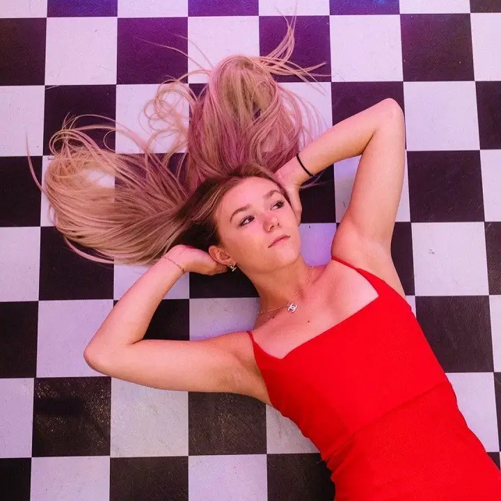 Katie Sigmond laying on a chessboard floor with her arms on her head.