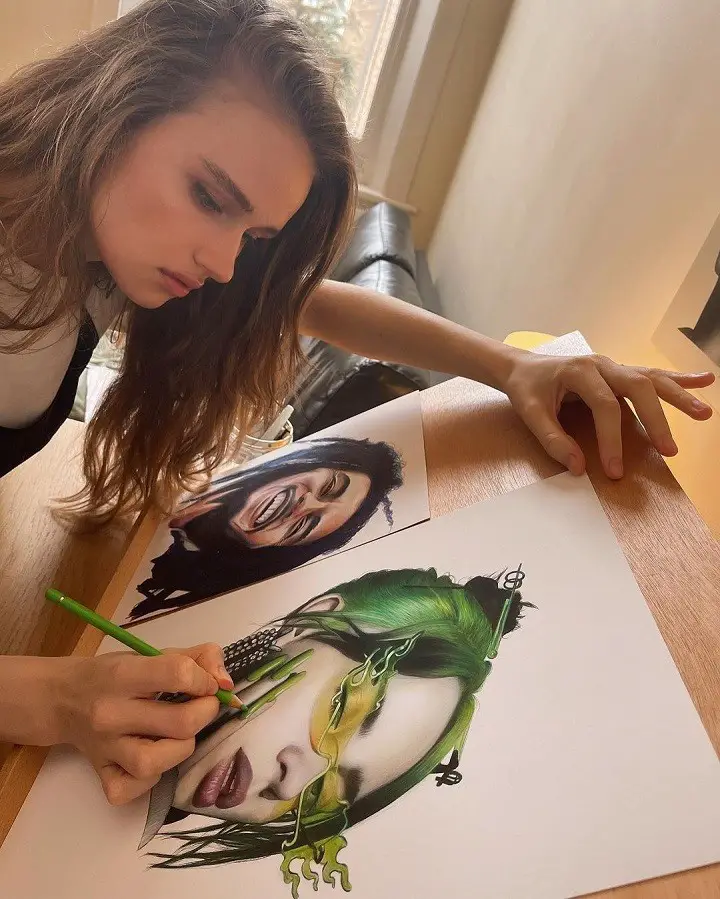 Julia Gisella applying the finishing touches on her art of Billie Eilish, with an art of Bob Marley also on the scene.