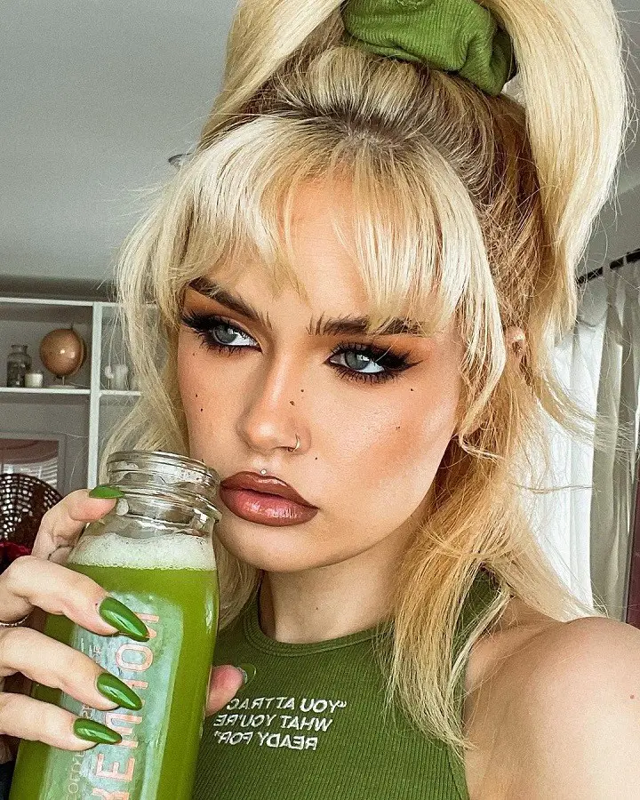 Ash Levi holding a green drink with freckled makeup on.