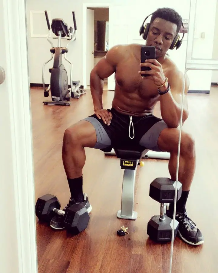 Chibuikem Uche taking a selfie in a mirror shirtless with headphones on during a workout session.