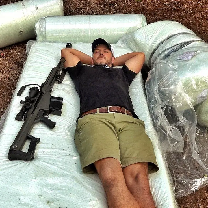 Matt Carriker with a gun beside on an outdoor floor bed.