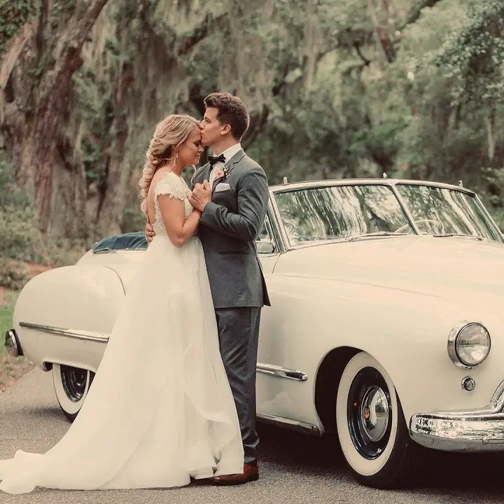 Barrett Carnahan (right) kissing his wife Nina Kubicki on her forhead beside a vintage car right after their wedding.