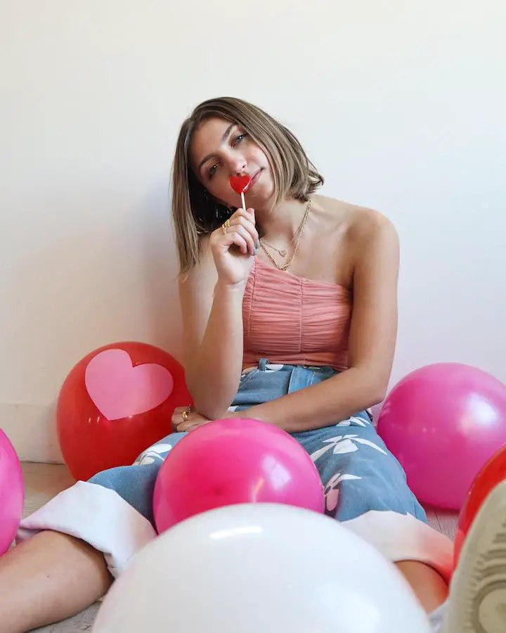 Kamri Noel McKnight posing in a Valentine's Day theme surrounding sitting with her back on the wall and a heart-shaped lollypop upto her face.