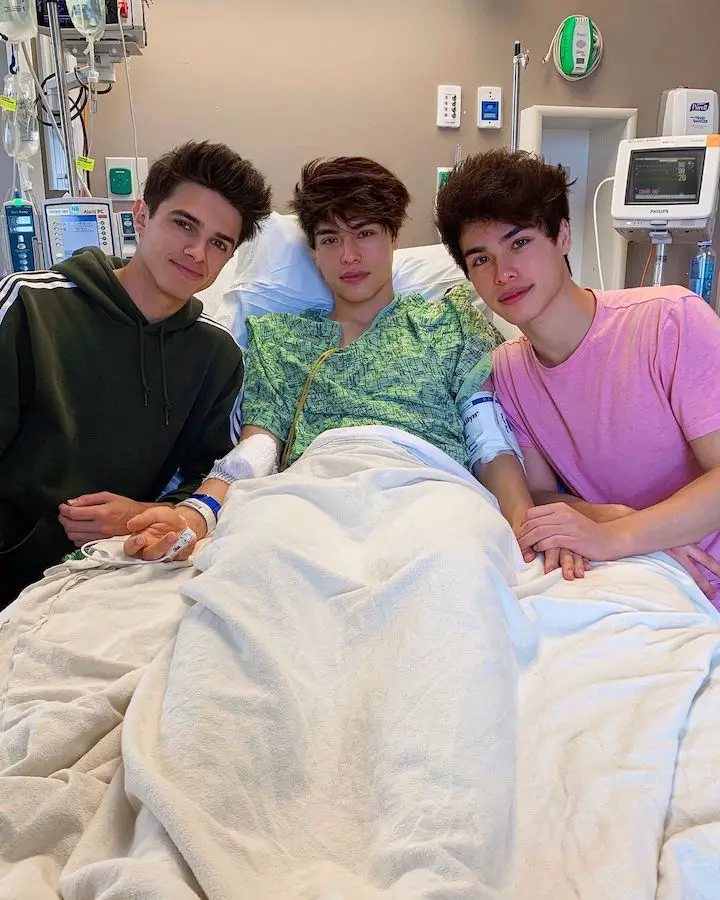 Alex Stokes (center) on a hospital bed during his apendicitis recovery with Bex Azelart (left) and his twin brother Alan Stokes (right) beside him.
