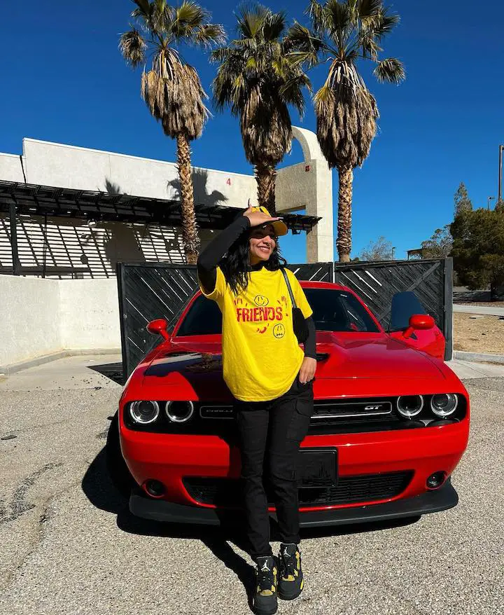 Scarlet May in a Yellow T-shirt standing in front of the hood of a Dodge car.