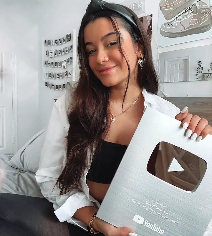 Carol Chaves holding a silver YouTube plaque for her 100,000 subscriber mark.