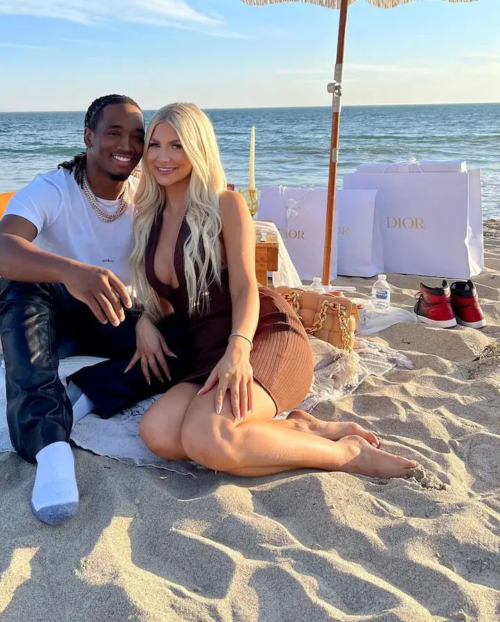 Charles Davis (left) and girlfriend Alyssa Hyde (right) sitting on the beach with Dior bags behind them.