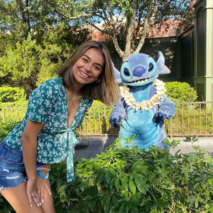 Giselle Lomelino crouching up to the level of a Disneyland employee in the Stitch character costume behind her to the right.