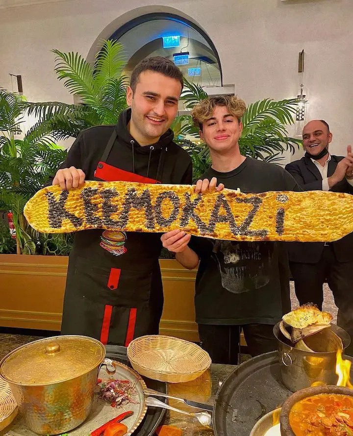 Keemokazi (right) with CZN Burak (left) holding a sign that says 'KEEMOKAZI' on some sort of food.