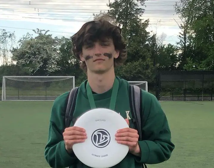 Rian McCririck holding a white frisbee with war paint on his face after a game of Ultimate Frisbee while still wearing a backpack.