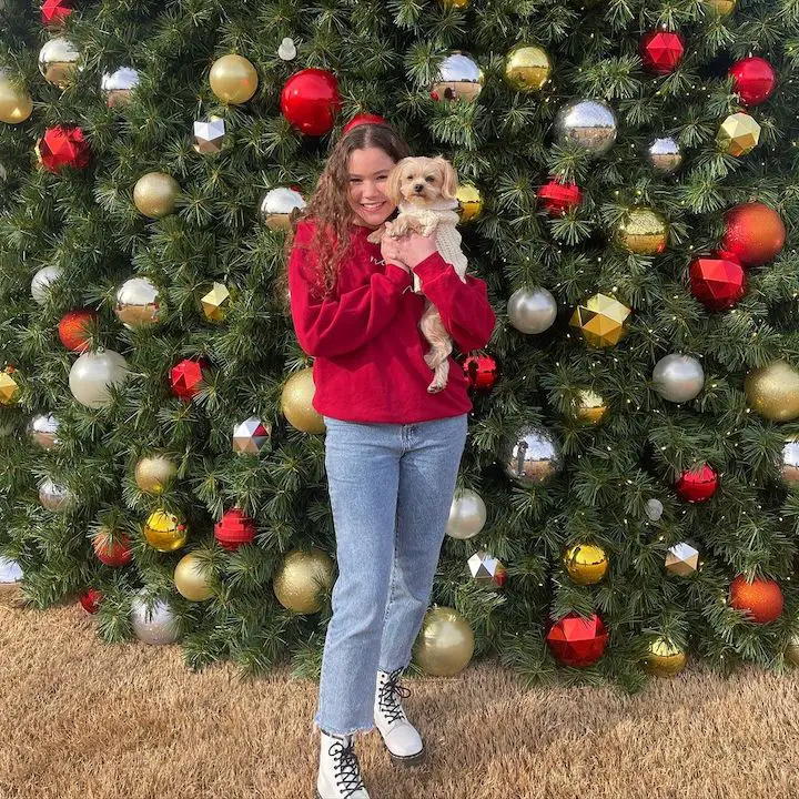 Sierra Haschak hugging a dog to her head level with a multiple christmas tree backdrop.