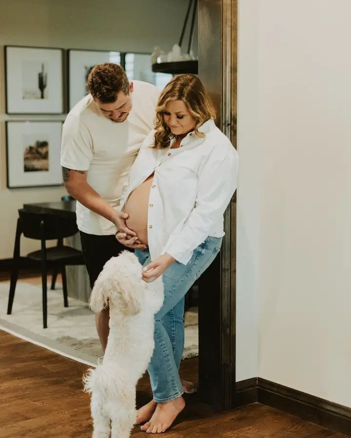 A pregnant Kendall Rae (right) coddling her dog leaping on her lap as her husband Josh Thomas (left) touched her belly for a romantic pose.