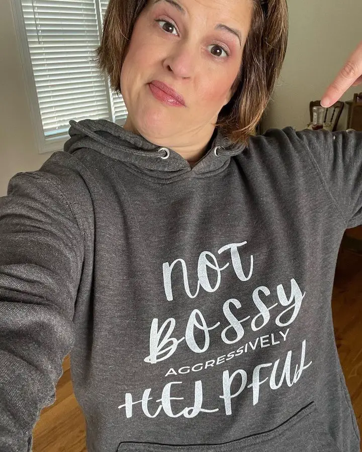 Laurel Beard taking a selfie while pointing to the print on her hoodie that says, "not bossy aggressively helpful" while making a smug face.
