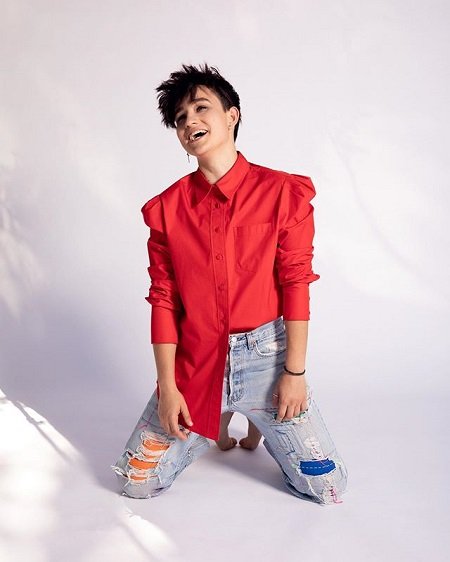 Bex Taylor-Klaus in a red shirt and ripped jeans. Their net worth will surprise you.