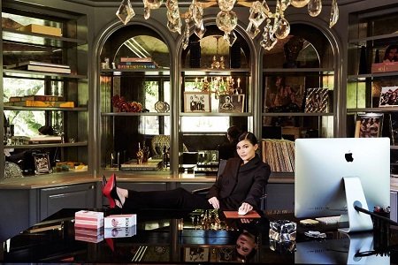 Kylie sitting in a businessman chair with her legs on the table and a bunch of stuff belonging to her mother in her home.