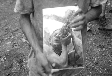 Photographer Moises Arias taking a Photography shot of himself in a mirror held by someone else, with his favorite camera..
