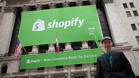 Shopify CEO Tobi Lütke outside the New York Stock Exchange. A huge green board with Shopify written on it is displayed behind him.