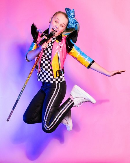 JoJo Siwa jumping up in the air with a mic stand in her hand.