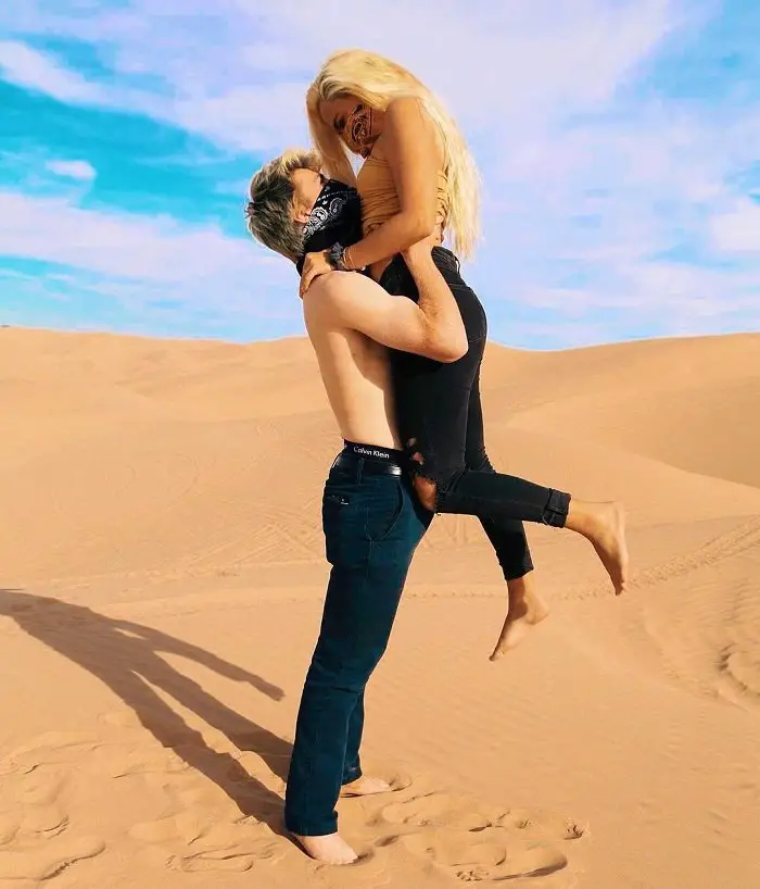 Kouvr Annon lifting girlfriend Kouvr Annon in the air in the desert with mouth covered with handkerchiefs.