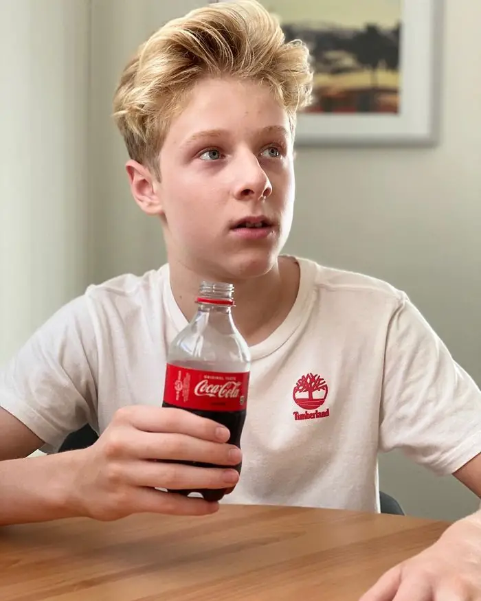 Lev Cameron looking away from the camera with an open plastic Coca Cola bottle.