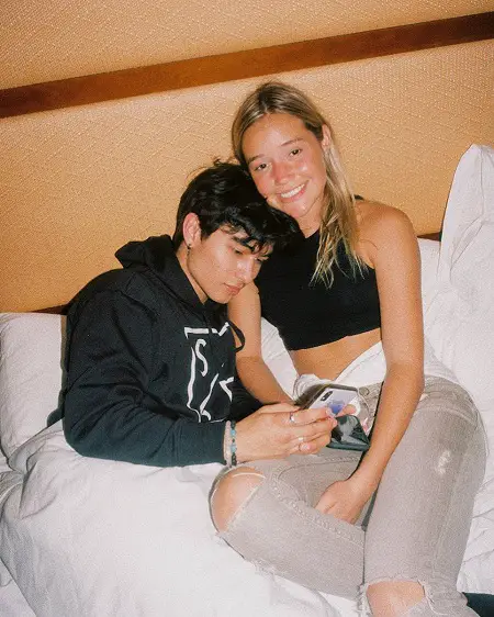 Kio Cyr using his phone beside girlfriend Olivia Ponton smiling at the camera.