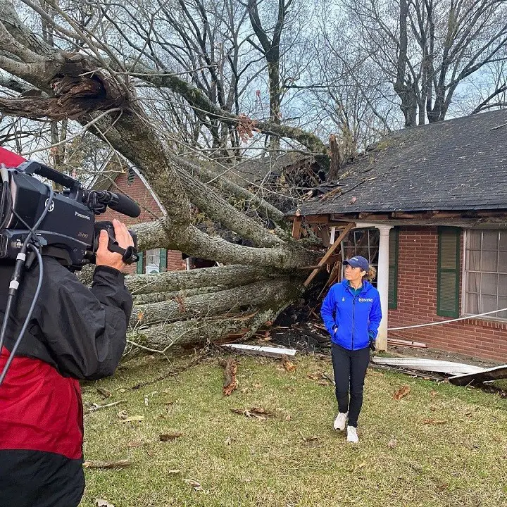 Ginger Zee at the scene after a disaster being filmed in front of a house toppled by a massive broken tree.