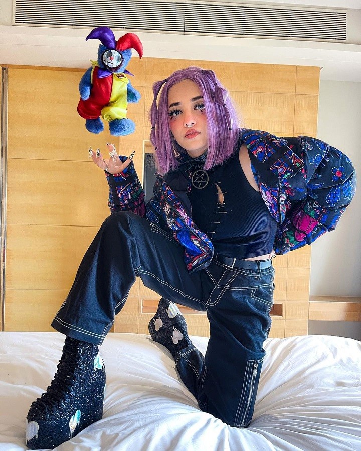 themermaidscales posing with boots on herr bed as if she is levitating a joker doll.