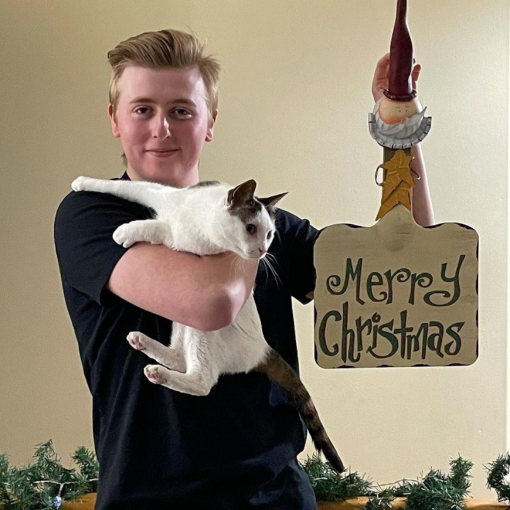 Luke Davidson posing with a cat and holding a 'Merry Christmas' sign.