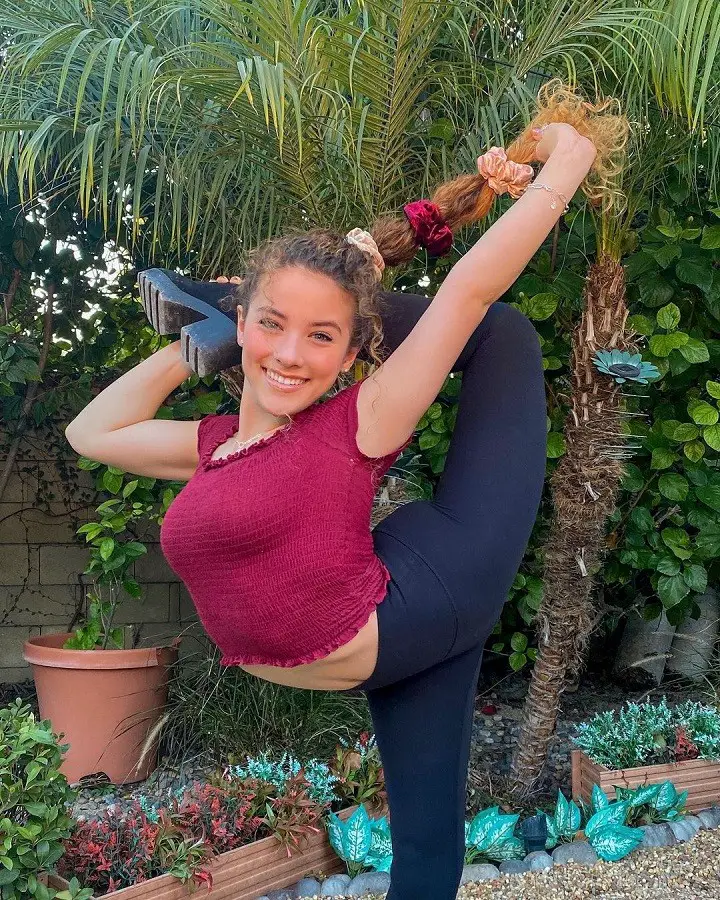 Sofie Dossi contorting her left leg over her shoulder while pulling her hair back.