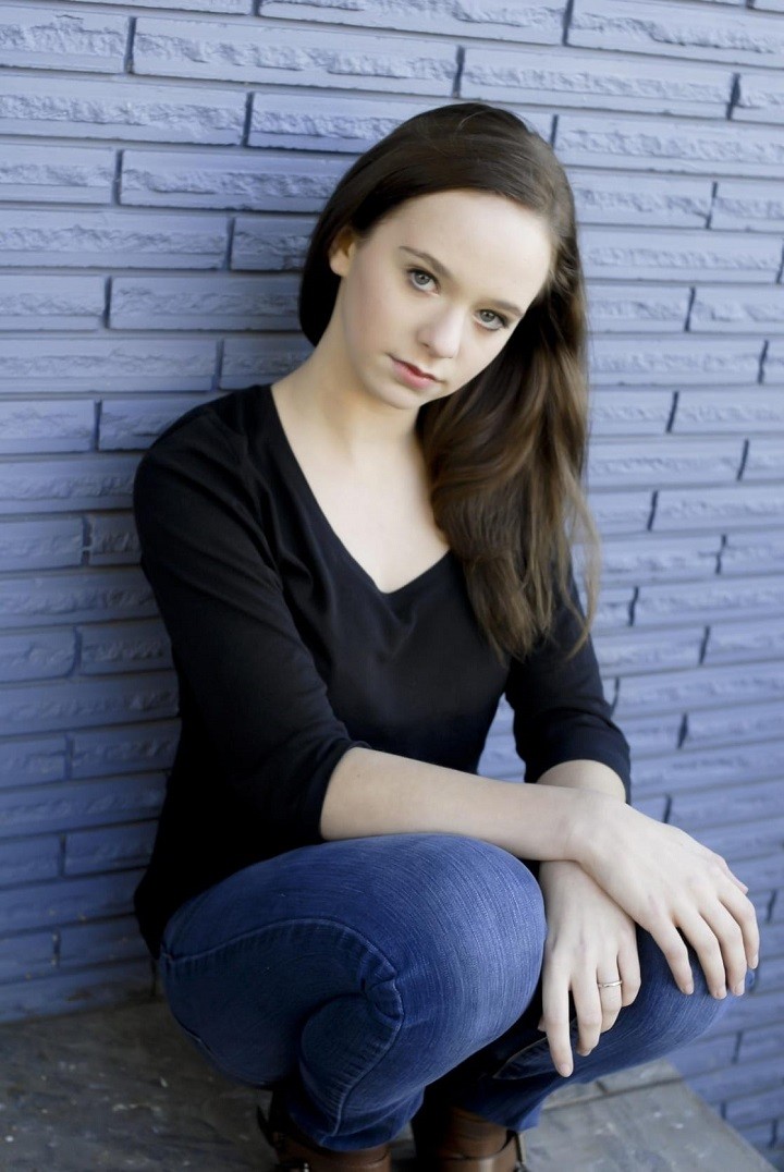 A young Jessica McLeod leaning against a blue-colored brick wall.