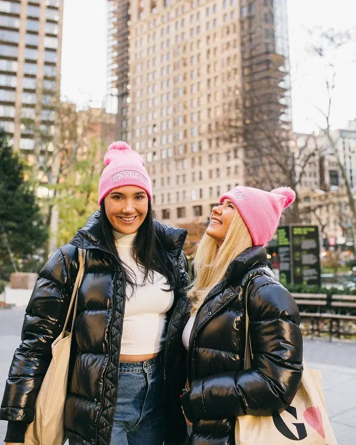Podcast partners Brooke Miccio (left) and Danielle Carolan (right) in matching outfits, and pink caps.