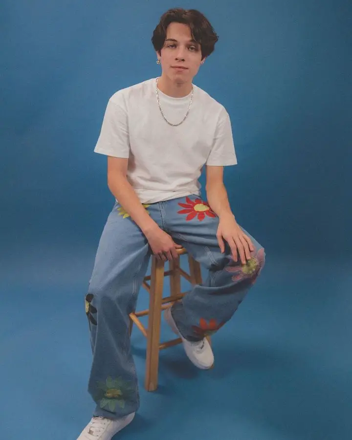 Matthew Sturniolo of the Sturniolo Triplets sitting on a tool for a pose in a blue room.