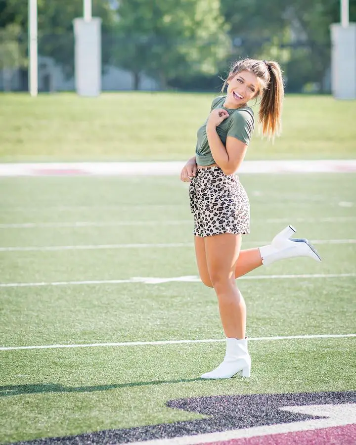 Tabitha Swatosh posing with the classic one leg stand with a smile and hand raised to her neck.