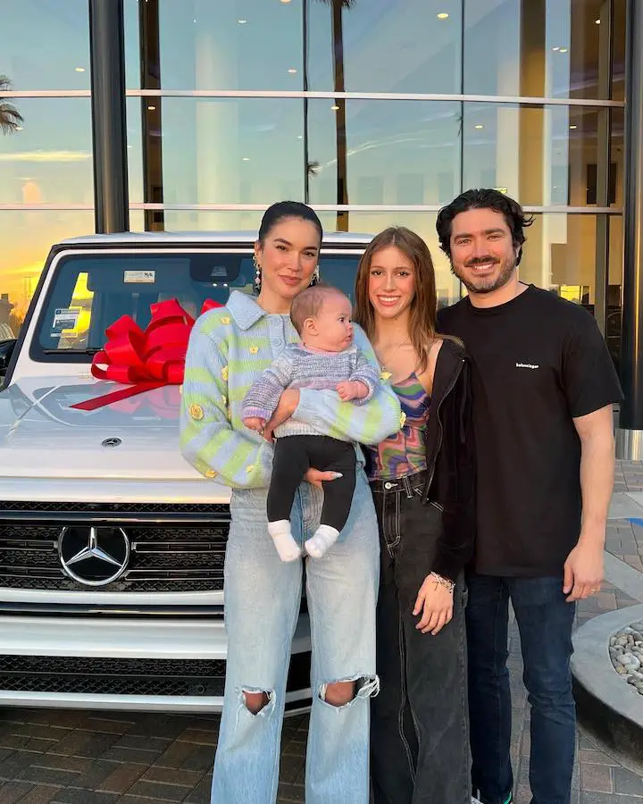 Brittany Xavier (left) holding her infant baby girl Poppy Wren with her first daughter Jadyn Xavier (center) and husband Anthony Xavier (right) in front of a brand new Mercedes.