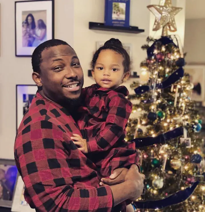 American Football running back LeSean McCoy holding his daughter up in front of a Christmas tree.