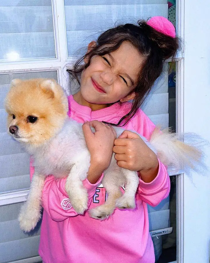 Solage Ortiz showing a cringed pose on her face while holding a carefully trimmed dog in her arms.