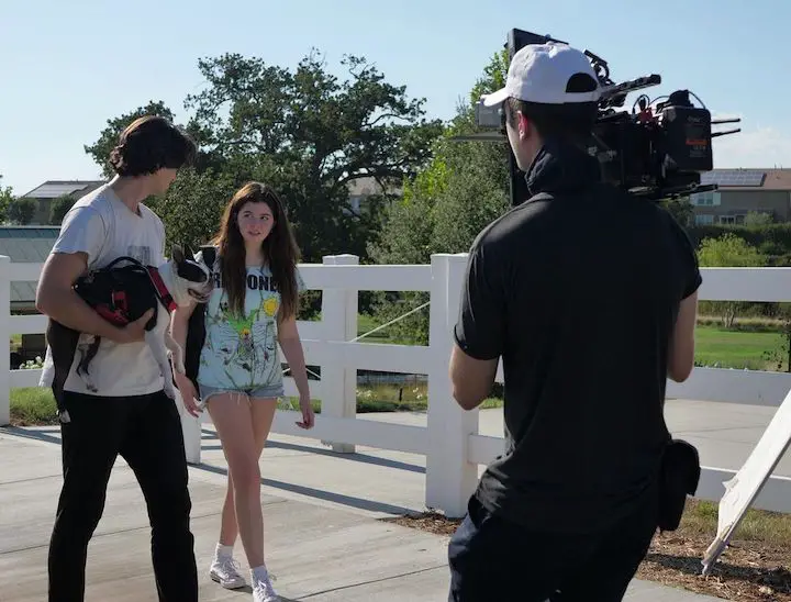 Addison Riecke (center) with her 'Maddie' co-star Larson Rainer (left) with his dog in his hands, walking on a bridge during a scene in 'Maddie' with a cameraman (right) also on the shot shooting the short movie.