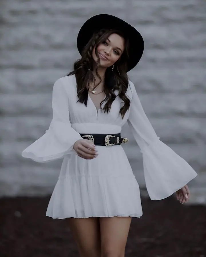 Signa Mae in a walking pose in a white dress and a hat with braided hair.