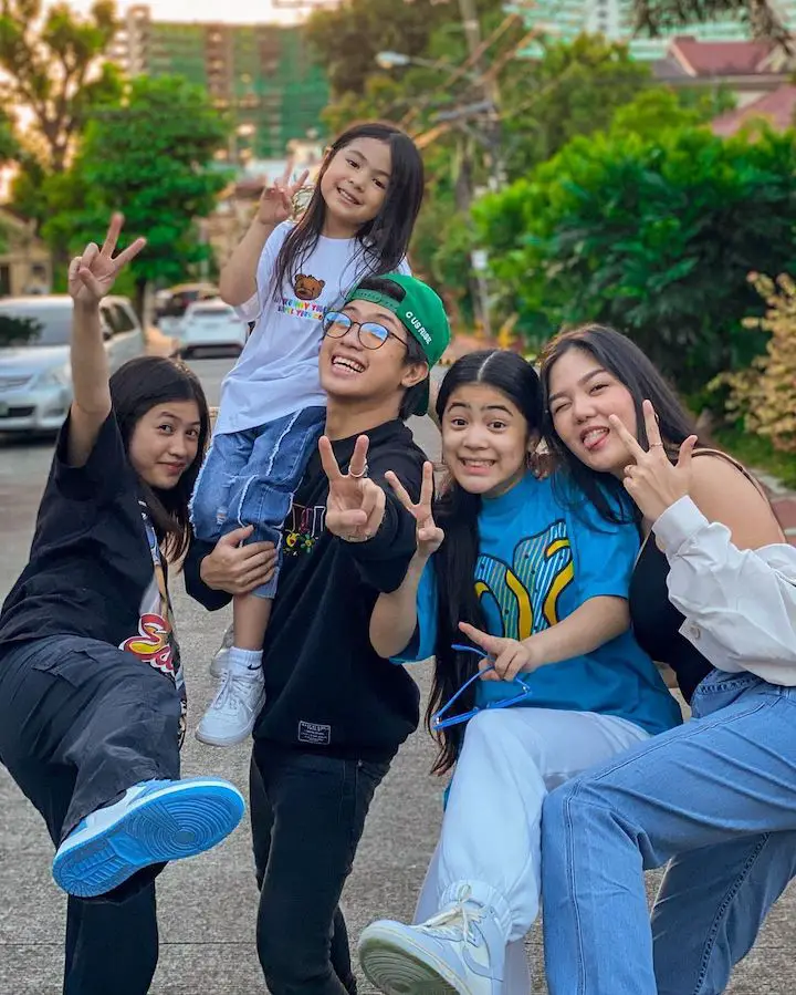 Natalia Guerrero (second from left) being carried by Ranz Kyle (center) alongside her sisters Chelsea Ongsee (far left), Niana Guerrero (second from right), and Niña Stephanie (right) all making peace symbols.