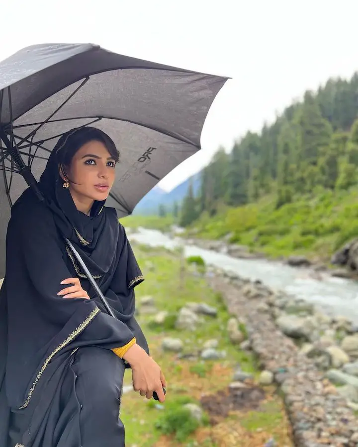 Samantha Ruth Prabhu in an all black outfit holding a big black umbrella alongside the river.