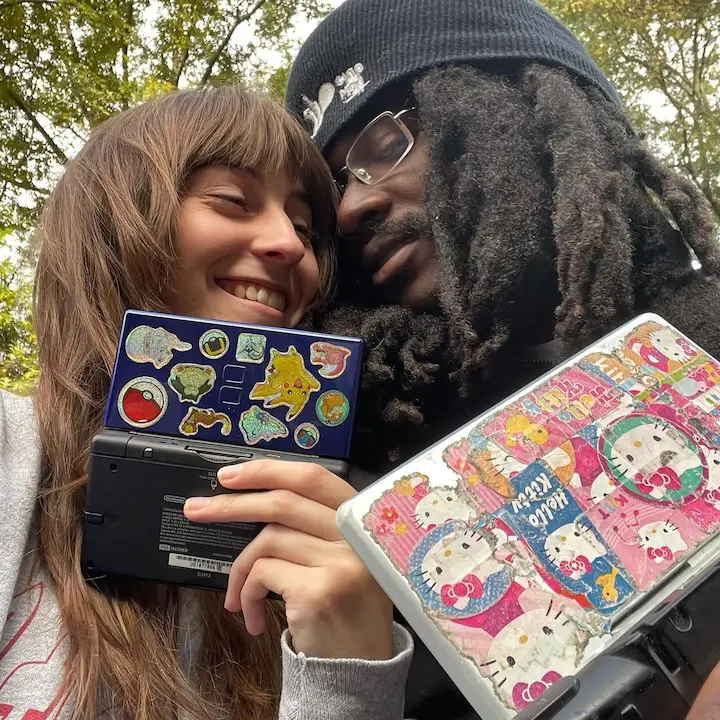 Singer Faye Webster taking a selfie with her boyfriend Boothlord displaying Nintendo's covered in stickers from popular cartoons Pokemon and Doraemon respectively.